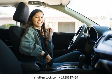 Portrait Of A Happy Adolescent Girl Putting On Her Safety Seatbelt And About To Start Her Car. Teen Girl Smiling And Getting Ready To Drive 