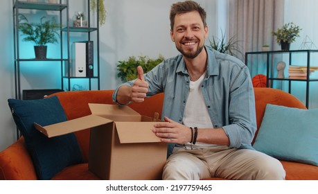 Portrait Of Happy Adult Man Unpacking Delivery Parcel Sitting At Home. Smiling Satisfied Young Guy Shopper, Online Shop Customer Opening Cardboard Box Receiving Purchase Gift By Fast Postal Shipping