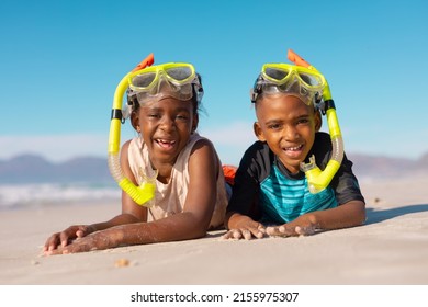 Portrait of happy african american boy and girl wearing snorkels and masks lying on sand against sky. summer, copy space, unaltered, beach, childhood, family, togetherness, enjoyment, holiday.