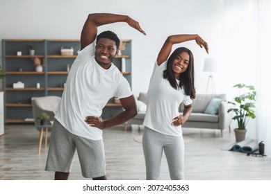 Portrait Of Happy African American Couple Doing Standing Side Bend Stretch Exercise, Working Out Together In Living Room At Home. Fitness Workout Motivation, Domestic Training Concept. Selective Focus