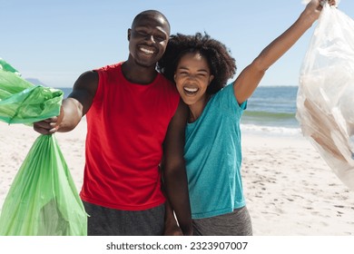 Portrait of happy african american couple cleaning sunny beach and collecting litter. Summer, lifestyle, free time, ecology, recycling and vacation, unaltered. - Powered by Shutterstock