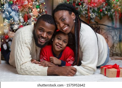 Portrait Of Happy African American Family On Christmas Eve, Lying On Floor Near Xmas Tree, Cuddling And Smiling At Camera