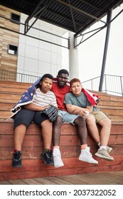 Portrait Of Happy African American Father Hugging Teenage Sons Covered With American Flag While They Sitting On Bleacher Bench