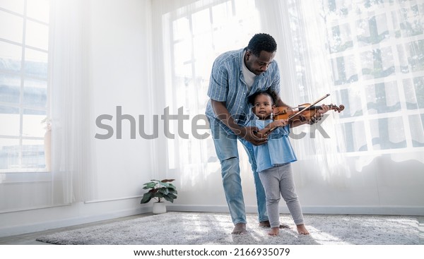 Portrait of happy African American father,\
teacher and little black girl daughter playing violins. Family\
leisure time doing hobby with music instrument. Love together\
fatherhood, Father\'s Day\
concept