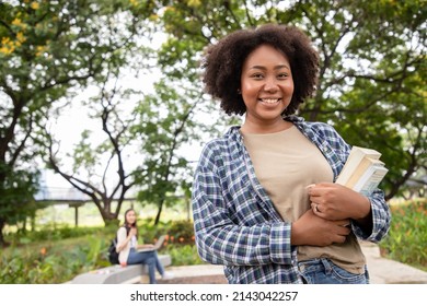 Portrait of a happy African American female student holding books and looking at natural outdoors with her friends at park. Prepare for college and university concept