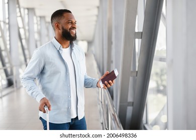 Portrait Of Happy African American Man Waiting For His Flight In Modern Airport. Smiling Black Guy Holding Passport With Ticket, Waiting For Departure, Looking Out Of Window, Free Space