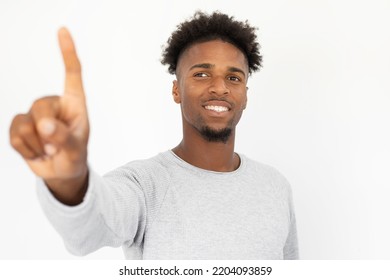 Portrait Of Happy African American Man Touching Invisible Wall. Young Bearded Guy Wearing White Sweater Pointing At Camera And Smiling Against White Background. Interactive Technology Concept