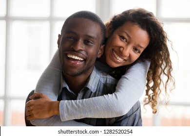 Portrait of happy african american mixed race couple embracing looking at camera, loving husband piggybacking wife in new home, smiling loving woman hugging black man, dating concept, headshot