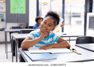 Portrait of happy african american schoolgirl sitting at desk in school classroom. Education, childhood, elementary school and learning concept.