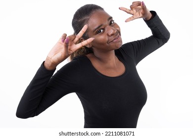 Portrait Of Happy African American Woman Showing Victory Sign. Young Female Model In Black Shirt Looking At Camera, Smiling And Doing Peace Sign. Studio Shot, Victory, Success, Optimism Concept.