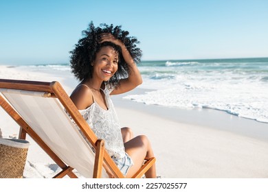 Portrait of happy african american woman sunbathing on wooden deck chair at tropical beach while looking at camera. Smiling black girl enjoying vacation at seaside with copy space. Woman relaxing.
