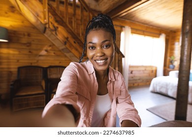 Portrait of happy african american woman spending time in log cabin and having video call. Log cabin, nature and lifestyle concept. - Powered by Shutterstock