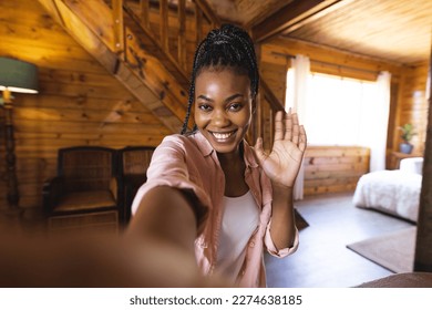 Portrait of happy african american woman spending time in log cabin and having video call. Log cabin, nature and lifestyle concept. - Powered by Shutterstock