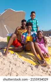 Portrait Of Happy African American Young Parents Relaxing With Son And Daughter At Beach Against Sky. Copy Space, Umbrella, Unaltered, Childhood, Family, Togetherness, Enjoyment, Holiday, Summer.