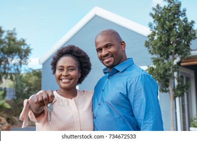 Portrait Of A Happy African Couple Standing Arm In Arm Together Outside Holding The Keys To Their New Home