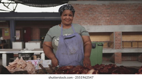 Portrait of a happy African female butcher wearing a headscarf in a township workshop, standing next to a table with fresh meat, slow motion - Powered by Shutterstock