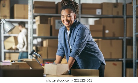 Portrait of a Happy African Small Business Owner Working on Laptop in Warehouse, Preparing Parcels for Delivery. Female Smile and Pose for Camera in Storeroom with Cardboard Boxes. - Powered by Shutterstock