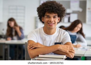 Portrait of happy african university student  in class looking at camera. Smiling young man at college leaning on stack of books with classmates in background. Satisfied african guy at college.