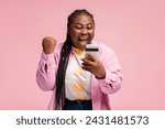 Portrait happy African woman holding mobile phone, sports betting, win money celebration success isolated on pink background. Overjoyed Nigerian female online shopping with sales. Good news concept 