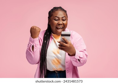 Portrait happy African woman holding mobile phone, sports betting, win money celebration success isolated on pink background. Overjoyed Nigerian female online shopping with sales. Good news concept  - Powered by Shutterstock