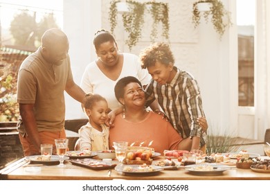 Portrait Of Happy African-American Grandmother Celebrating Birthday With Family During Dinner Outdoors, Lit By Sunlight