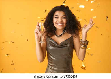 Portrait of happy African-American woman with glass of champagne and falling confetti on color background