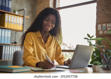 Portrait of happy afro american young businesswoman write note work laptop consultant indoors in office workplace