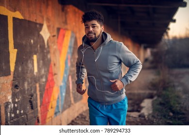 Portrait Of Happy Afro-american Attractive Active Runner Man Jogging Outside On Abandon Place With Earphones.