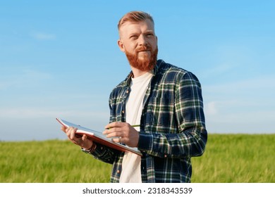 Portrait of a happy agronomist with a notebook in a wheat field. A farmer with a beard and a shirt prepares the field for the future harvest - Shutterstock ID 2318343539