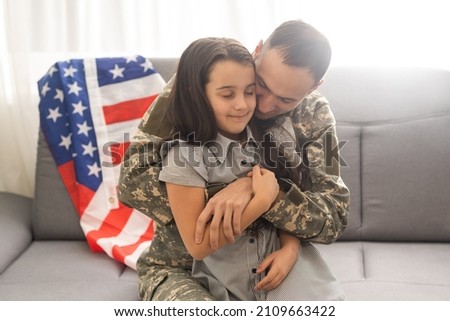 Portrait of happy american family father in military uniform and cute little girl daughter with flag of United States hugging and smiling at camera