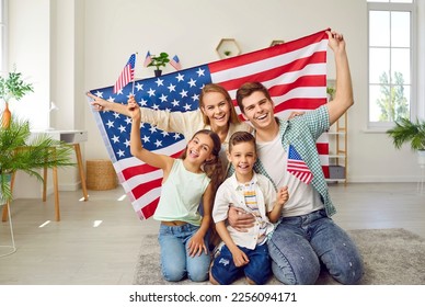 Portrait of happy American family with USA flag. Mother, father their son and daughter sitting with American flag at home. Family celebrating 4th of July Independence Day - Powered by Shutterstock