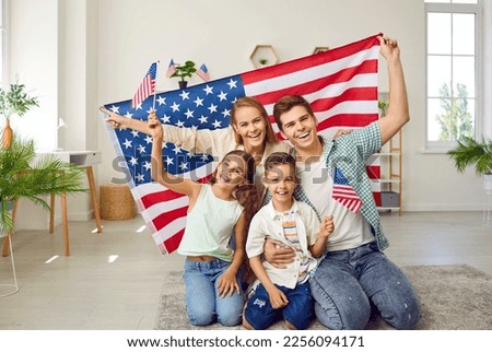 Portrait of happy American family with USA flag. Mother, father their son and daughter sitting with American flag at home. Family celebrating 4th of July Independence Day