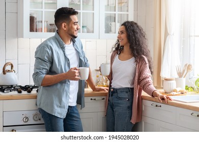 Portrait Of Happy Arab Couple Drinking Coffee And Chatting Together In Kitchen Interior, Young Middle Eastern Lovers Enjoying Hot Drink At Home, Holding Cups And Smiling To Each Other, Free Space
