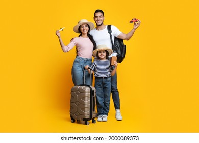 Portrait Of Happy Arab Family With Little Daughter Ready For Vacation, Cheerful Middle Eastern Parents And Their Child Standing With Suitcases, Pasports And Travel Souvenirs Over Yellow Background