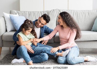 Portrait Of Happy Arab Family Spending Time Together At Home, Cheerful Middle Eastern Parents Having Fun With Their Daughter, Tickling Little Child And Laughing, Enjoying Domestic Leisure, Free Space