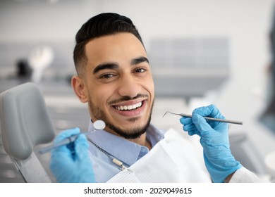 Portrait Of Happy Arab Man Sitting At Dentist Chair In Modern Clinic And Smiling At Camera, Middle Eastern Male Patient Enjoying Dental Treatment With Professional Stomatologist, Closeup Shot