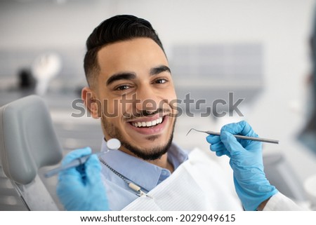 Portrait Of Happy Arab Man Sitting At Dentist Chair In Modern Clinic And Smiling At Camera, Middle Eastern Male Patient Enjoying Dental Treatment With Professional Stomatologist, Closeup Shot