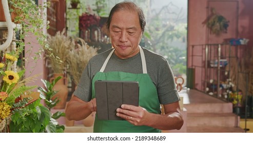 Portrait Of A Happy Asian American Business Owner Holding Tablet Smiling At Online Orders. Male Entrepreneur Of Small Business Store Using Modern Tablet Digital Device To Manage Inventory