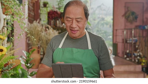 Portrait Of A Happy Asian American Business Owner Holding Tablet Smiling At Online Orders. Male Entrepreneur Of Small Business Store Using Modern Tablet Digital Device To Manage Inventory