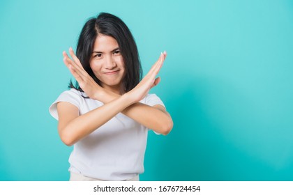 Portrait Happy Asian Beautiful Young Woman Unhappy Or Confident Standing Wear White T-shirt, She Holding Two Crossing Arms Say No X Sign, Studio Shot On Blue Background With Copy Space For Text