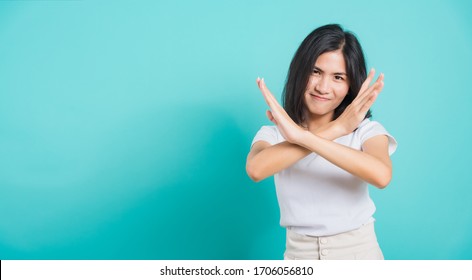 Portrait Happy Asian Beautiful Young Woman Unhappy Or Confident Standing Wear White T-shirt, She Holding Two Crossing Arms Say No X Sign, Studio Shot On Blue Background With Copy Space For Text