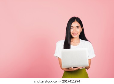 Portrait von glücklicher asiatischer schöner junger Frau, selbstbewusstes, lächelndes Gesicht, das mit einem Laptop hält, der auf die Kamera schaut, Studioaufnahme einzeln auf rosafarbenem Hintergrund, mit Kopienraum
