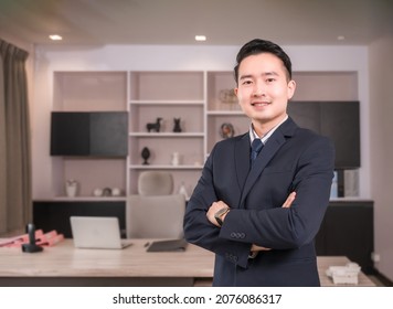 Portrait Of Happy Asian Businessman CEO In Suit With Arms Crossed And Looking At Camera In Modern Room At Workplace. Handsome Male Executive Financial Director Standing And Smiling Success In Office.