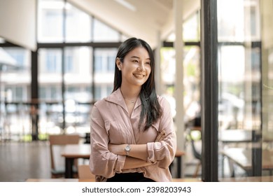 Portrait of happy asian businesswoman standing arms crossed in office. Looing outside mirror. - Powered by Shutterstock