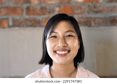 Portrait of happy asian casual businesswoman smiling against brick wall in office. Casual office, confidence, business and work.