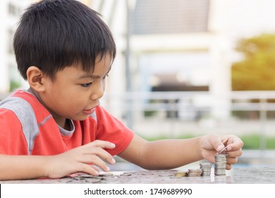 Portrait Of Happy Asian Child Boy Counting The Coins. Childhood Put The Money On The Table. Kid Saving Money For The Future Concept. Children Learning.