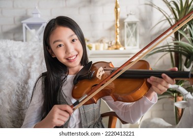 Portrait Of Happy Asian Child Girl Sitting Playing Violin Instrument While Learning Music For Talent Upskills Education At Home. Cute Kid Violinist Classical Musician Smile And Look Camera At School.