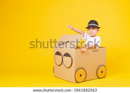 Portrait happy Asian cute little children boy smile so happy wearing white T-shirt driving car creative by cardboard and pointing finger, studio shot on yellow background with copy space