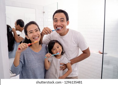 portrait of happy asian family brush their teeth together in bathroom sink. parent brush teeth and take care of kid