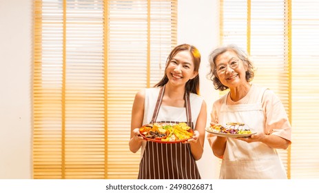 Portrait of Happy Asian family enjoy indoor healthy lifestyle cooking and having dinner together at home. Senior mature mother and adult daughter preparing vegan food vegetables salad in the kitchen. - Powered by Shutterstock